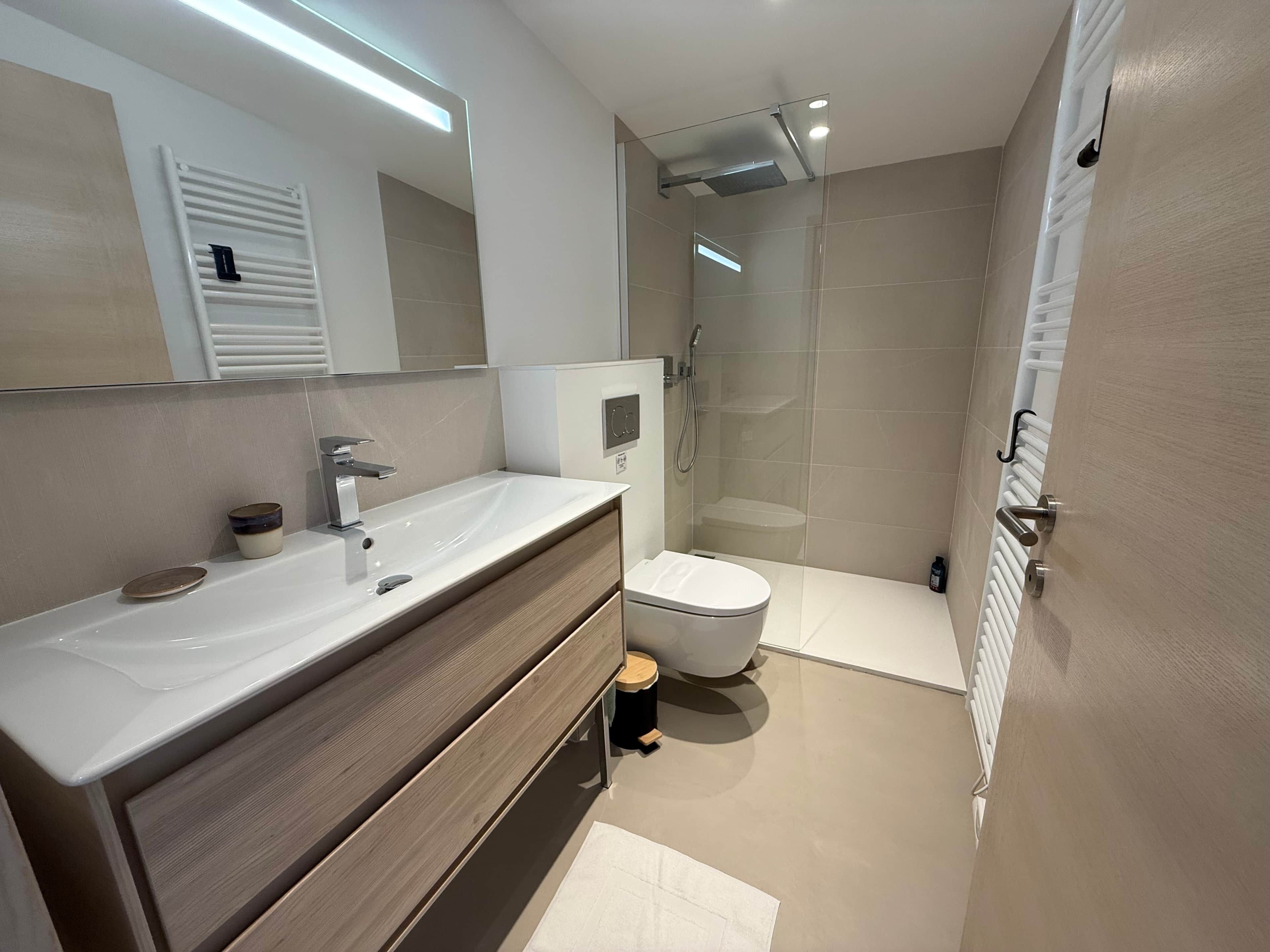 Une salle de bain moderne équipée d’un meuble-lavabo, de toilettes et d’une douche.