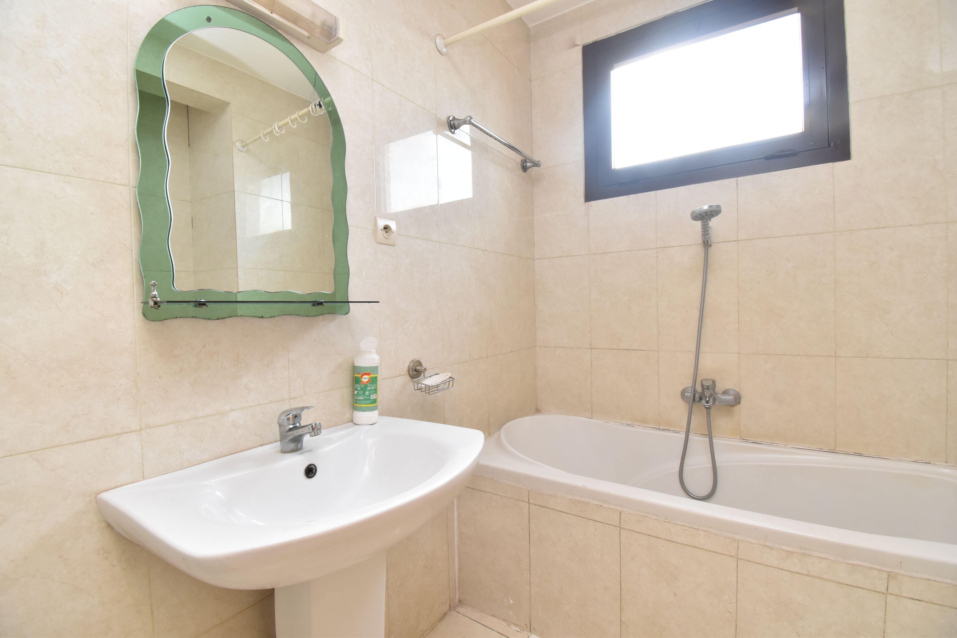 A bathroom with a sink, mirror, shower, and window.