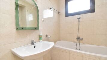 A bathroom with a sink, mirror, shower, and window.