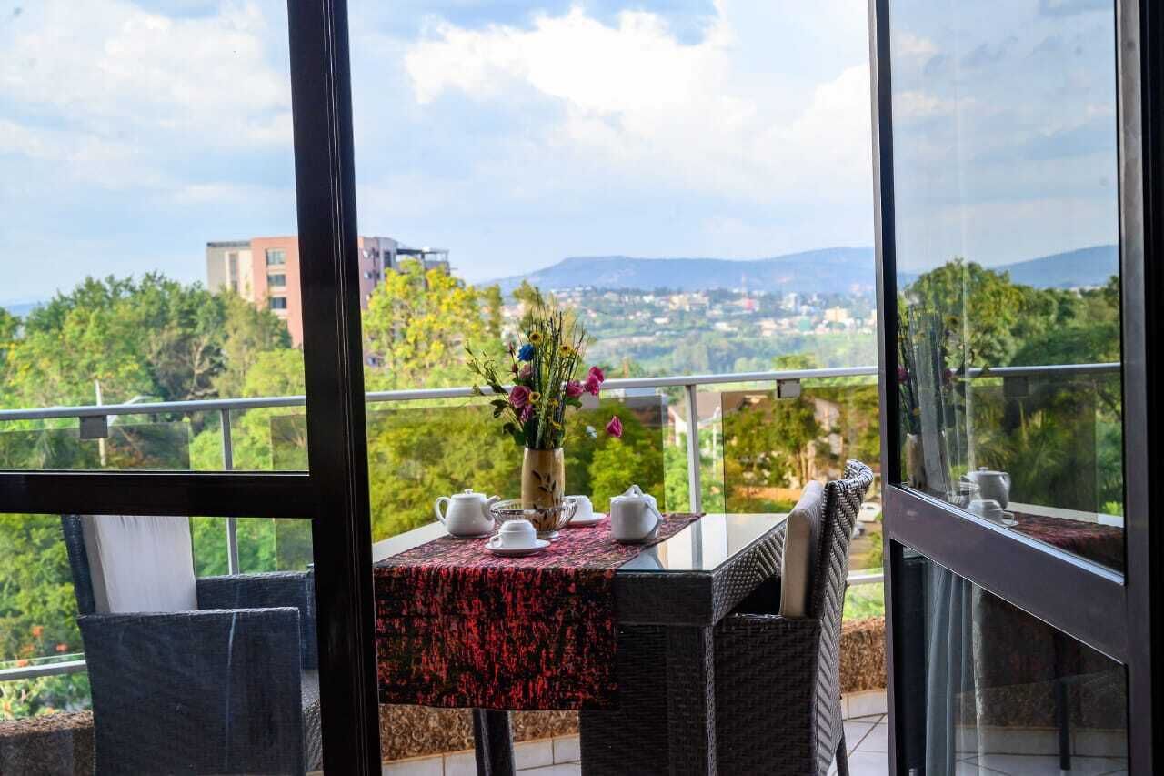 A balcony with a table set for tea, a vase with flowers, and a cityscape view.