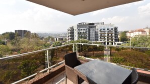Un balcón con una mesa y sillas, con vista a un paisaje urbano con edificios modernos y zonas verdes.