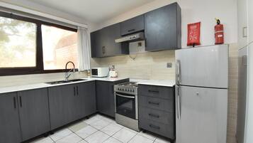 Una cocina moderna con armarios grises, un refrigerador de acero inoxidable, un horno empotrado y un microondas.