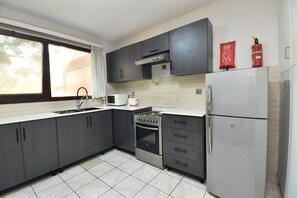 A modern kitchen with grey cabinets, a stainless steel refrigerator, a built-in oven, and a microwave. - Residency by La Maison Royale (Kigali)