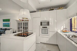 A modern kitchen with white cabinetry, a built-in oven, and a dining area with a white table and black leather sofa. - Vacation Home 'Bungalow Meloneras' with Sea View, Wi-Fi and Air Conditioning (Maspalomas)