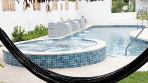 Ein Pool mit Wasserfall, umgeben von einer weißen Mauer und viel Grün.