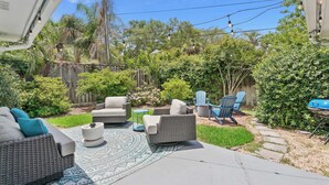 Eine Terrasse mit Gartenmöbeln, einem Grill und einem Gartenbereich mit verschiedenen Pflanzen und einem Holzzaun.