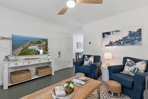 Ein Wohnzimmer mit Fernseher, einem blauen Sofa, einem Couchtisch und einem Gemälde an der Wand.