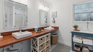 Un bagno con due lavandini, un mobile contenitore, uno specchio e una finestra decorata con stelle marine.