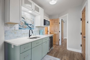 A kitchen with teal cabinets, a white countertop, a microwave, and a wooden door. - The Turtles Nest on Mulat Bay in Avalon Beach (Avalon)