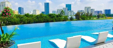 Una piscina con sillas de descanso, rodeada de vegetación y un horizonte urbano al fondo.