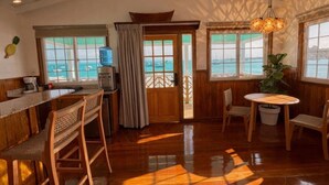 A room with a wooden floor, a bar area with chairs, a table, and a view of the sea through large windows. - Double Waterfront Bungalows (#1 & #4) (Bocas del Toro)