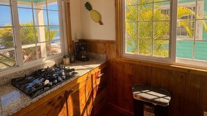 A kitchen with wooden cabinets, a gas stove, a coffee maker, and a trash can. - Double Waterfront Bungalows (#1 & #4) (Bocas del Toro)