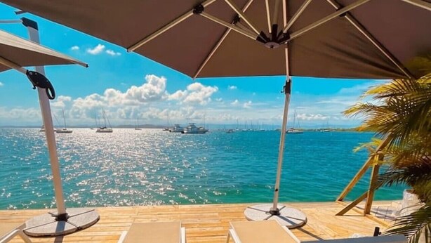 A wooden deck with white lounge chairs and a large umbrella, overlooking a calm sea with boats. - Double Waterfront Bungalows (#1 & #4) (Bocas del Toro)
