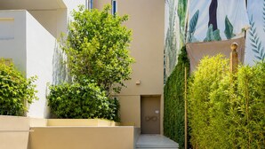 A modern building with a narrow pathway leading to a door, surrounded by greenery and a clear blue sky. - Krabo Villa & Spa (Vouliagmeni)