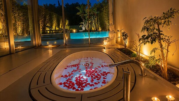 A spa area with a hot tub surrounded by plants, a glass ceiling, and a view of a pool. - Krabo Villa & Spa (Vouliagmeni)