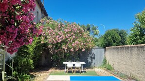 Ein Pingpongtisch in einem Garten mit Tisch und Stühlen, umgeben von viel Grün und blauem Himmel.