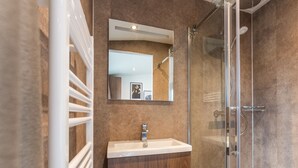 A bathroom with a glass shower enclosure, a white sink with a wooden cabinet, and a mirror above the sink.