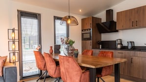 A modern kitchen with wooden cabinets, a dining table with orange chairs, and a pendant light.