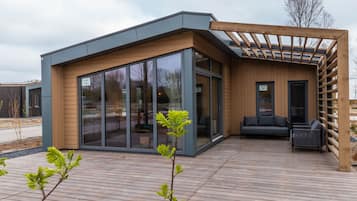 Une maison moderne dotée d’une terrasse en bois, de grandes portes-fenêtres coulissantes et d’un espace salon intégré.