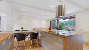 Een moderne keuken met een houten keukeneiland, zwarte stoelen en uitzicht op groen.