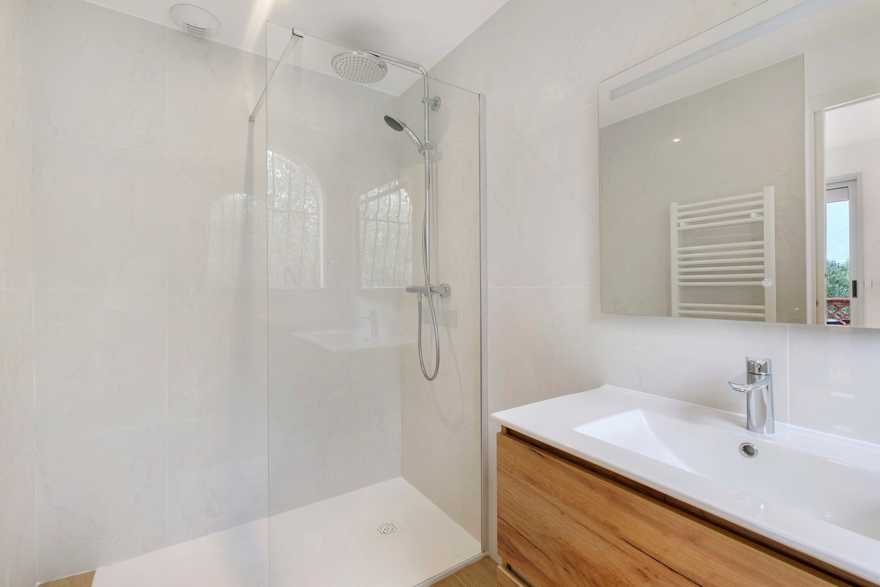 A modern bathroom with a glass-enclosed shower, a white sink, and a wooden vanity.