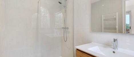 A modern bathroom with a glass-enclosed shower, a white sink, and a wooden vanity.
