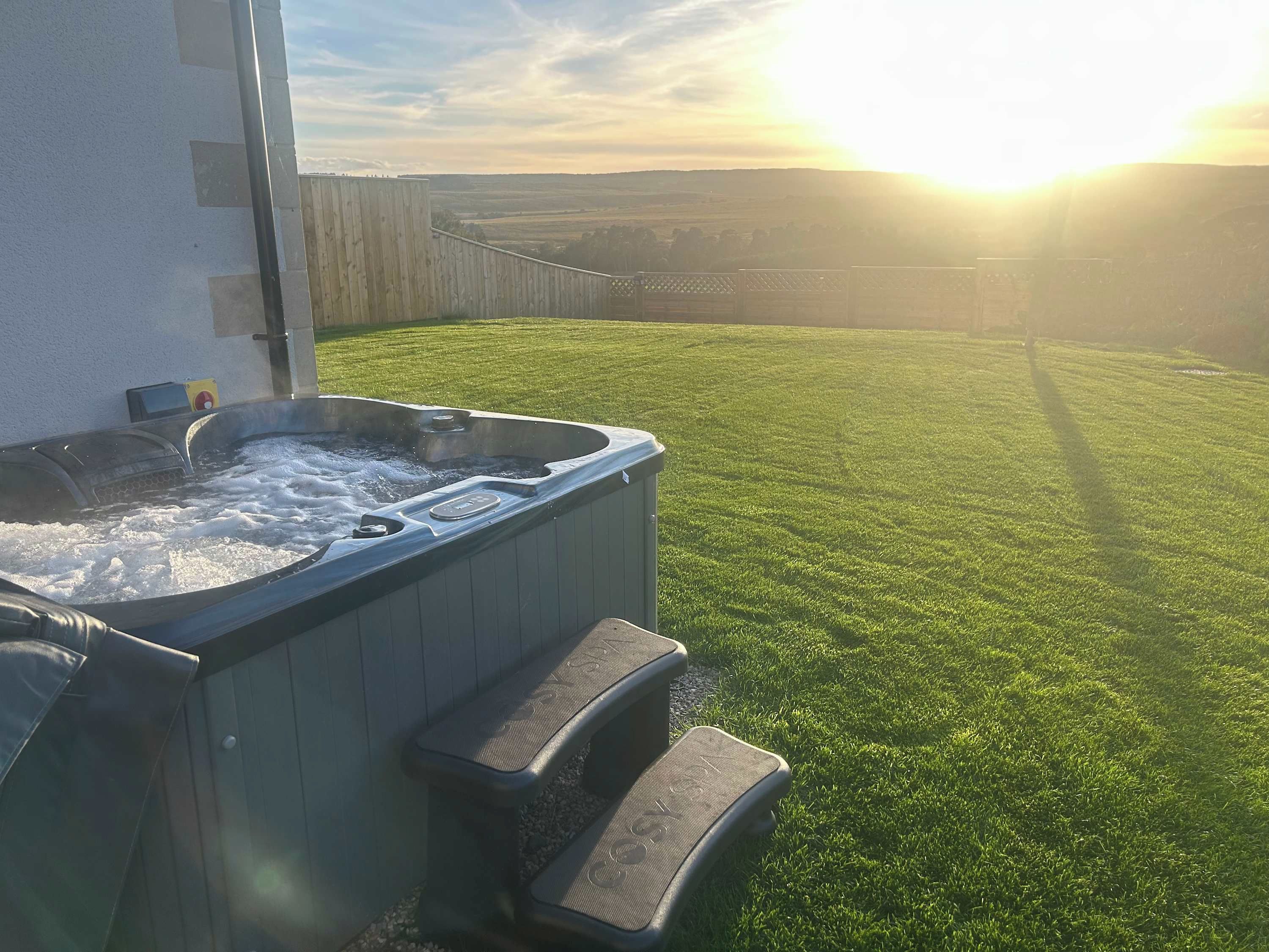 A hot tub with steps leading up to it, situated on a well-manicured lawn with a view of a distant landscape.