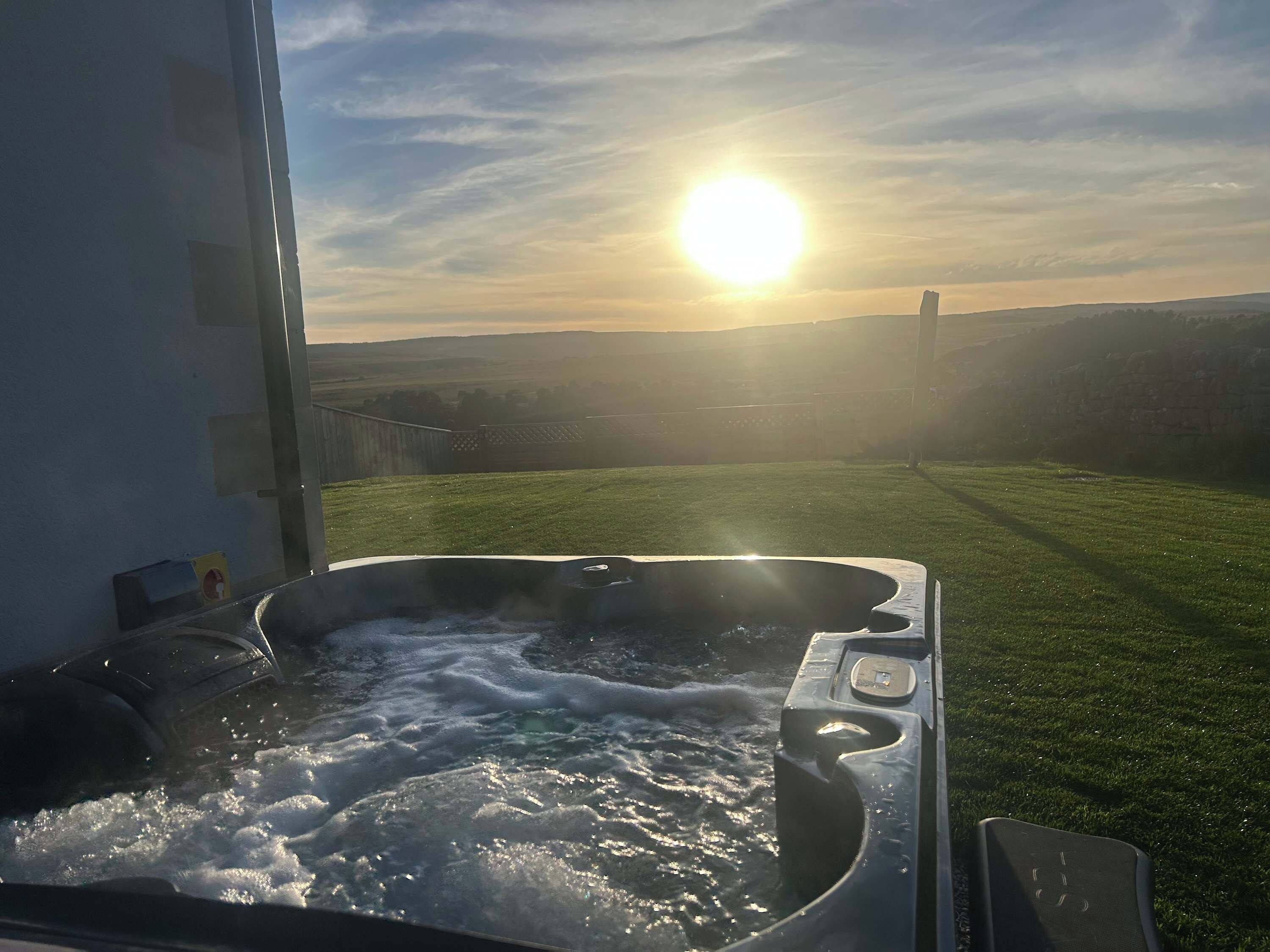 A hot tub with a view of the sunset over a grassy field.