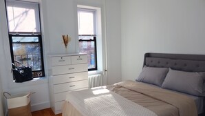 Une chambre à coucher avec un lit, une commode, un radiateur et des fenêtres.