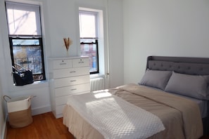 Une chambre à coucher avec un lit, une commode, un radiateur et des fenêtres.