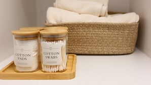 Deux boîtes étiquetées « cotons démaquillants » et « cotons-tiges » sont posées sur un plateau en bois, avec un panier tressé en arrière-plan.