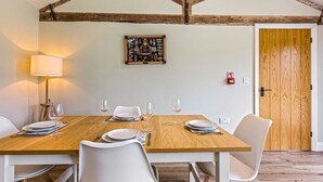 Un comedor con una mesa de madera dispuesta para cuatro, sillas blancas, un cuadro colgado en la pared y una puerta de madera.