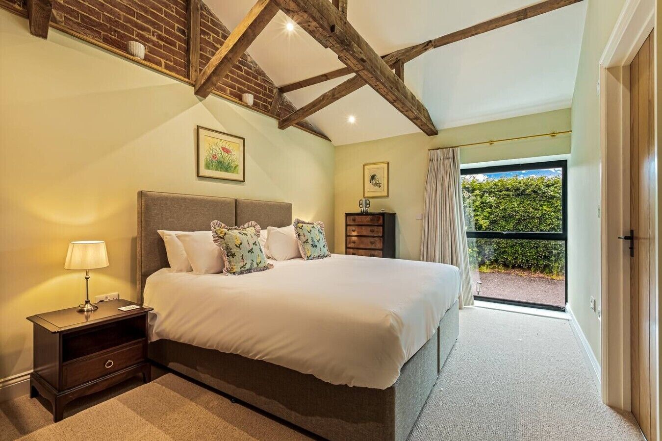 A bedroom with a bed, nightstand, dresser, and a view of a garden through a sliding door.