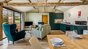 Un interior rústico con vigas de madera a la vista, una zona de estar acogedora, una cocina y una mesa de comedor para dos personas.