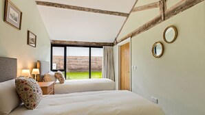 Un dormitorio con dos camas, una mesita de noche, una lámpara, una ventana que da a una valla de madera y dos espejos fijados a la pared.