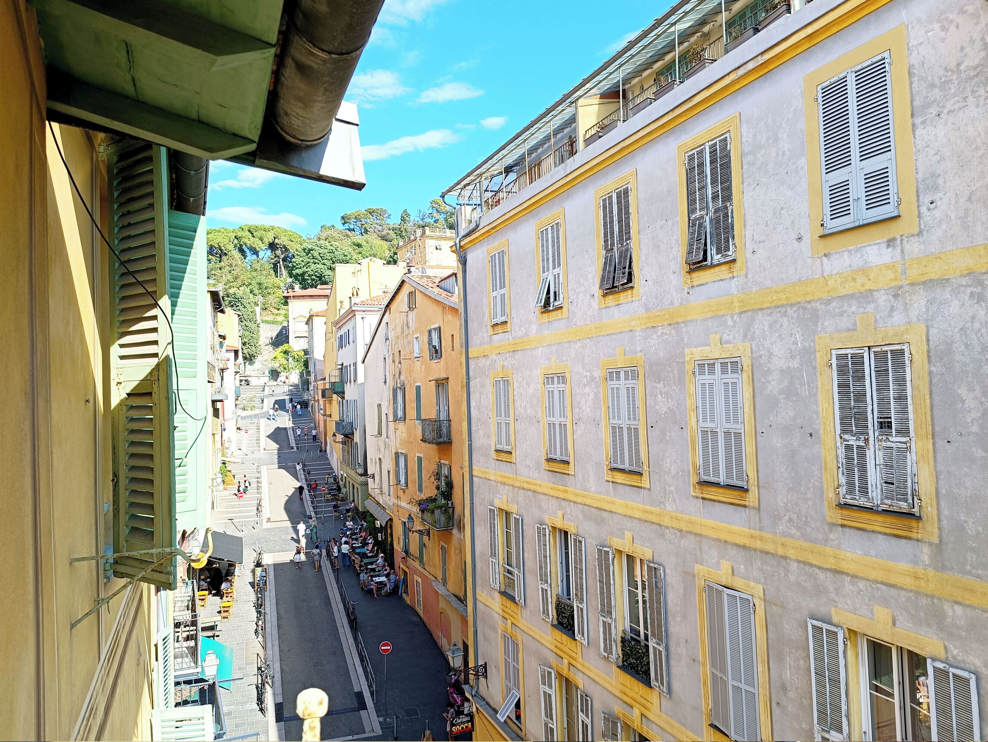 Eine schmale Straße mit Gebäuden an beiden Seiten, mit Balkonen und blauem Himmel.