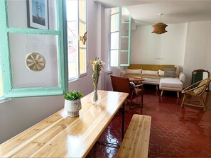 Een kamer met een houten tafel, een bank en een stoel. Er is een raam met uitzicht op gebouwen.