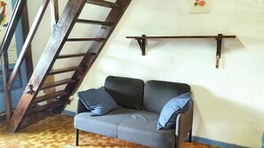 A room with a grey sofa, a wooden ladder, and a white wall with a shelf. - Studio with balcony (Six-Fours-les-Plages)