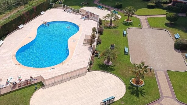 An aerial view of a swimming pool with a surrounding deck, palm trees, and a circular lawn area. - Apartment in Mandelieu-la-Napoule (Mandelieu-la-Napoule)
