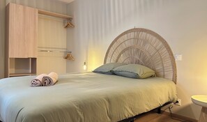 Ein Bett mit einem gewobenen Kopfteil, ein Nachttisch mit einer Lampe und ein Holzschrank.
