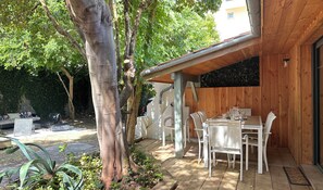 Ein Essbereich im Freien mit einer Holz-Pergola, weißen Stühlen und einem Tisch für vier Personen.
