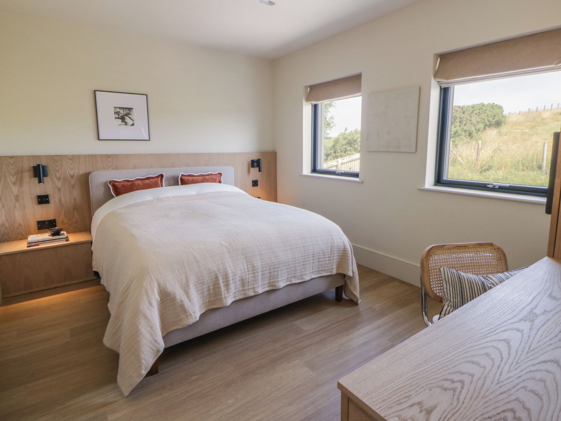 Une chambre à coucher avec un grand lit, des tables de chevet, une chaise et une fenêtre donnant sur un beau paysage.