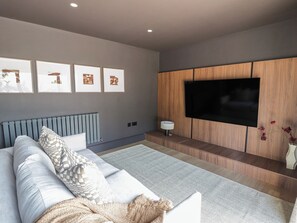 Un salon moderne avec un canapé gris, un téléviseur à écran plat fixé sur un mur recouvert de panneaux en bois, et des œuvres d’art encadrées accrochées au mur.