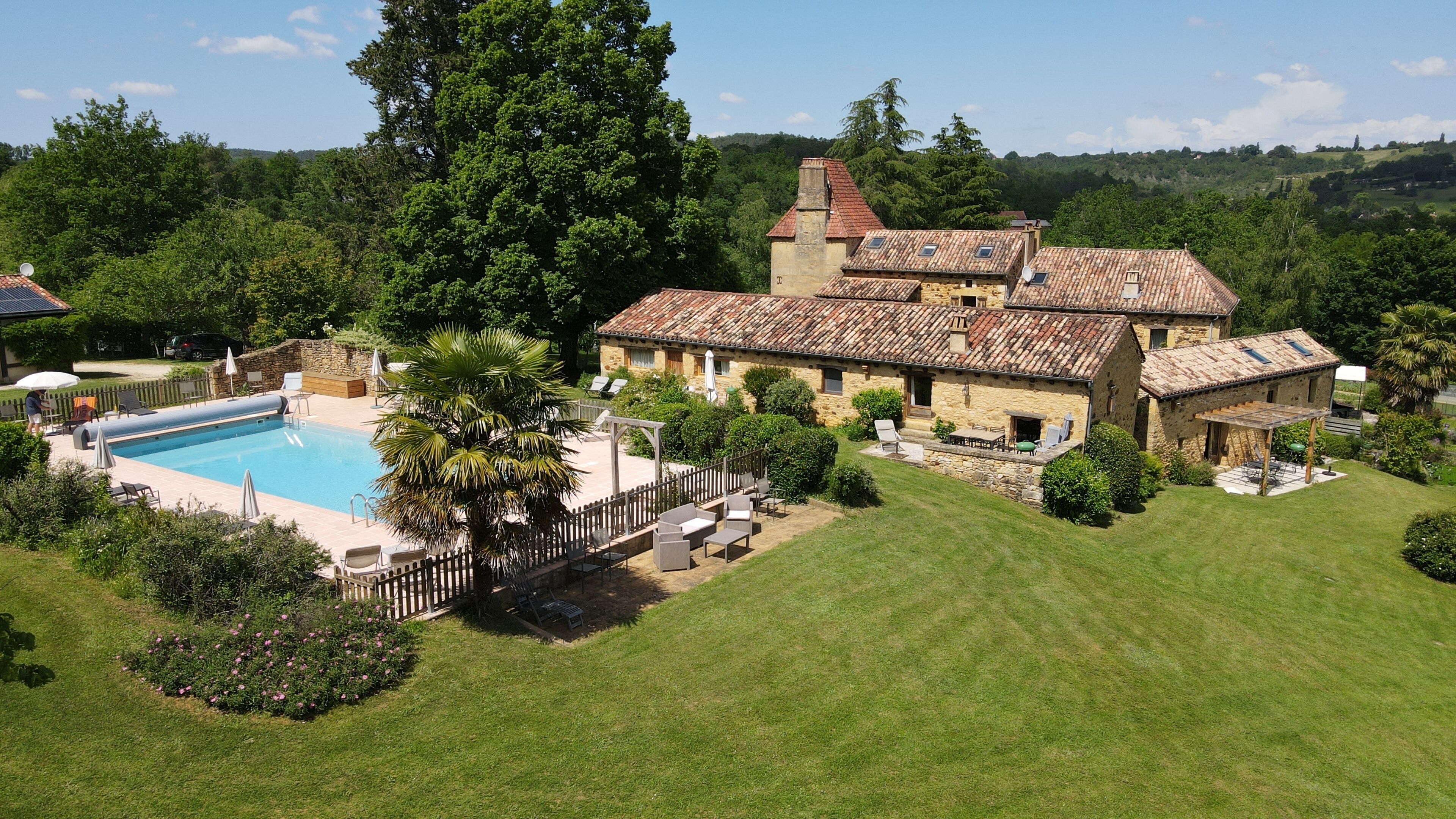 Un bâtiment en pierre doté d’une piscine, entouré d’une pelouse bien entretenue et d’arbres.