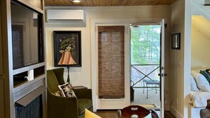 Une pièce chaleureuse avec un plafond en bois, une cheminée, un fauteuil vert, un canapé et une porte donnant sur l’extérieur.