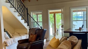 Un vaste espace de vie doté d’un plafond en bois, d’un canapé en cuir, d’un fauteuil marron et d’un escalier avec une rampe en fer forgé.