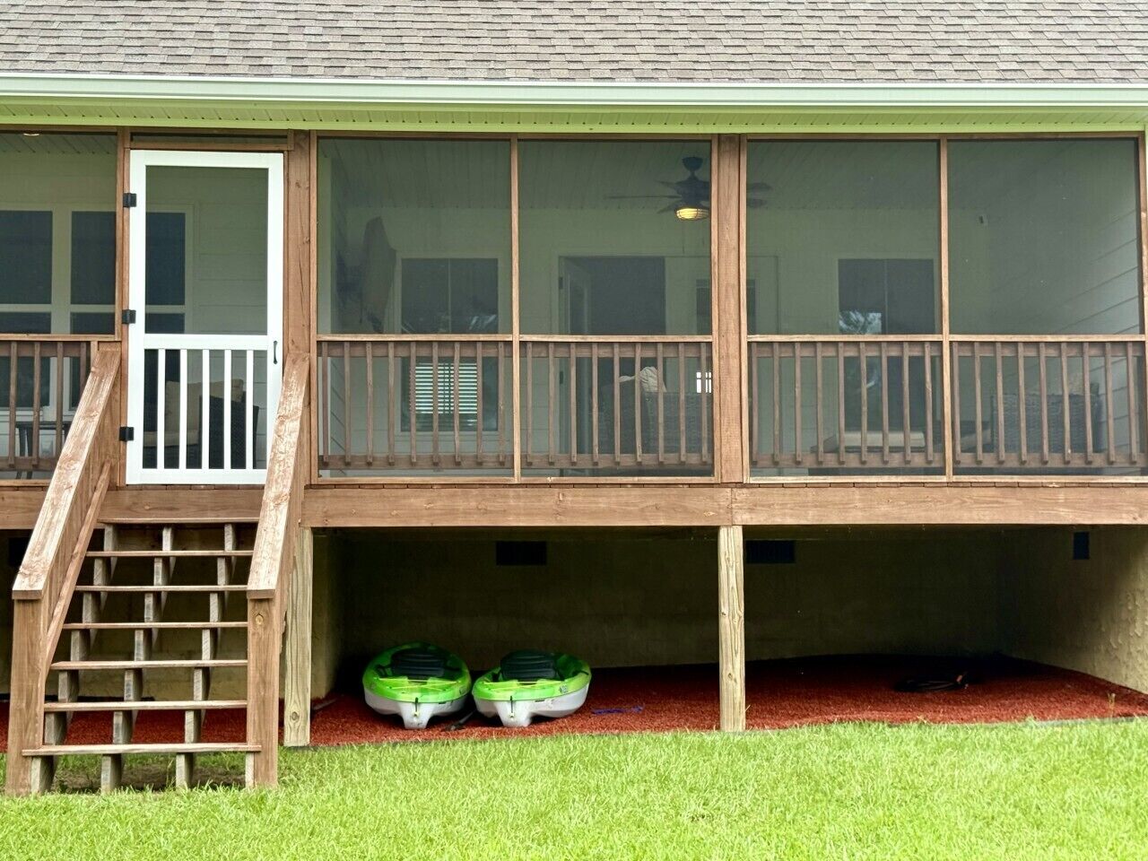 Un bâtiment à deux étages doté d’une terrasse en bois, d’un escalier menant à une porte, et de deux bateaux verts situés au rez-de-chaussée.