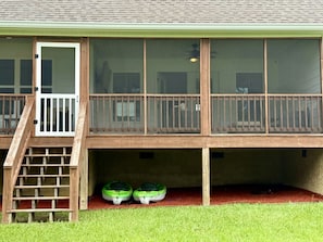 A two-story building with a wooden deck, a set of stairs leading to a door, and two green boats on the ground floor.