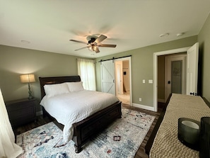 A bedroom with a bed, a ceiling fan, a nightstand, a lamp, a door, and a carpet.