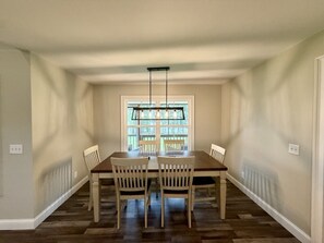 A dining room with a rectangular table and four chairs, a window with blinds, and a hanging light fixture.